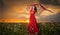 Fashionable beautiful young woman in long red dress posing outdoor with cloudy dramatic sky in background. Attractive brunette