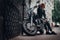 Fashionable biker dressed in a black leather jacket and jeans sitting on his retro motorcycle on an old Europe street.