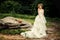 Fashionable bride in a lush white dress is standing by a large stone.