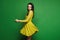 and fashionable brunette model girl with blue eyes and bright makeup in short stylish yellow dress spin around at green backg