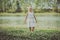 Fashionable child in white dress dancing in grass by the river and posing in summer time