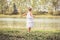 Fashionable child in white dress dancing in grass by the river and posing in summer time