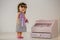 Fashionable doll with purple bow standing next to the toy dresser