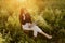 Fashionable elegant girl working on laptop and sitting on rustic chair in warm sunshine in summer meadow at sunset. Freelance.