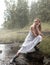 A fashionable girl in a dress and rubber boots sits on a rock