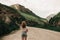 Fashionable girl in white clothes standing on the road in the highlands . green grass and mountains