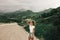 Fashionable girl in white clothes standing on the road in the highlands . green grass and mountains