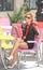 Fashionable lady with little black dress and red scarf sitting on chair in restaurant, outdoor shot in sunny day. Young blonde