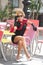 Fashionable lady with little black dress and red scarf sitting on chair in restaurant, outdoor shot in sunny day. Young blonde