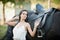Fashionable lady with white bridal dress near brown horse in nature. Beautiful young woman in a long dress posing with a horse