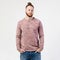 Fashionable man with beard and bun hairstyle dressed in pock-marked long sleeve sweater and jeans poses in the studio on