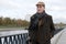 Fashionable mature man wearing woolen coat and hat walking along canal quay  bicycle during overcast autumn day