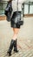 Fashionable modern girl in a skirt of black leather on a high waist and high boots on a heel posing on the street