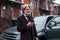 Fashionable senior man with gray hair and beard standing with phone near his car on the street