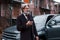 Fashionable senior man with gray hair and beard standing with phone near his car on the street