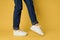 Fashionable shoes white sneakers legs yellow background cropped view