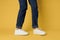 Fashionable shoes white sneakers legs yellow background cropped view