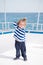 Fashionable small baby boy on yacht in marine shirt, pants