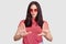 Fashionable woman being dissatisfied with something, shows refusal gesture, keeps palms in front, wears sunglasses, pink t shirt,