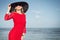 Fashionable woman with black summer hat and red dress on the beach