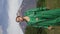 Fashionable woman model in green leather coat walking in forest on background of volcano. Vertical video