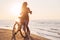 Fashionable woman riding bicycle on the beach at sunset