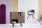 Fashionable wooden commode next to grey chair on white platform in modern interior