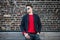 Fashionable young adult stylish man posing outdoors wearing red pulower, jeans, cotton jacket and sunglasses.