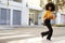 Fashionable young African American woman with afro hair running across the street, full length, close up