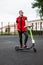 Fashionable young man in a red vest in black jeans in sneakers in sunglasses stands with a modern electric scooter