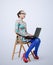 Fashionable young woman in dress and glasses sitting on chair with a laptop