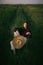 Fashionable young woman posing in summer countryside. Creative image. Stylish elegant girl holding straw hat and sitting on rustic