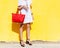 Fashionista shopaholic posing in a light summer dress and a red big handbag on a yellow wall background