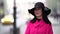 Fashionista is walking in city at autumn day, woman is wearing black hat and bright pink coat