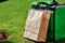 Fast delivery. Green thermal backpack and paper bag standing on the green grass outdoors, close up shot