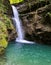 Fast flow of water a forest waterfall flows into azure calm water against a weathered stone gutter wall gorge