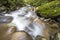 Fast flowing river stream with smooth silky water falling from big stones in beautiful waterfalls on bright sunny summer day