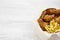 Fast food: fried chicken drumsticks, spicy wings, French fries and tender strips in paper box over white wooden surface, view from