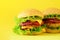 Fast food - juicy hamburgers on yellow background. Take away meal. Unhealthy diet concept with copy space