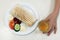 Fast food. Shaurma or doner on a white plate, next to a piece of cucumber and tomato with mayonnaise and ketchup. The boy`s hand