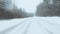 Fast maneuvering flight along the road surrounded by trees, close to the ground in snowfall. Snowflakes fall right into