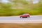 Fast moving red car on asphalt road. Panning shot