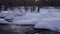 A fast river among white snowdrifts in a forest at sunset