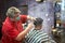 Fat concentrated barber cutting the hair of an asian client in a barber shop
