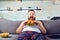 Fat funny man in pajamas eating a burger on the sofa at home.