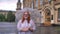 Fat ginger girl with glasses is standing in park in rainy weather, holding umbrella, watching at camera, smiling