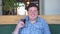 Fat happy man holding a glass of soft drink cola and laughing, sitting in cafe. Beverage