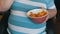 Fat, lazy man is eating potato chips sitting on a chair. A huge belly of a man under a striped T-shirt. Fast food, not
