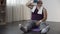 Fat male in sportswear sitting on mat and drinking water after hard workout