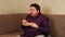 Fat man eats fast food while watching tv at home